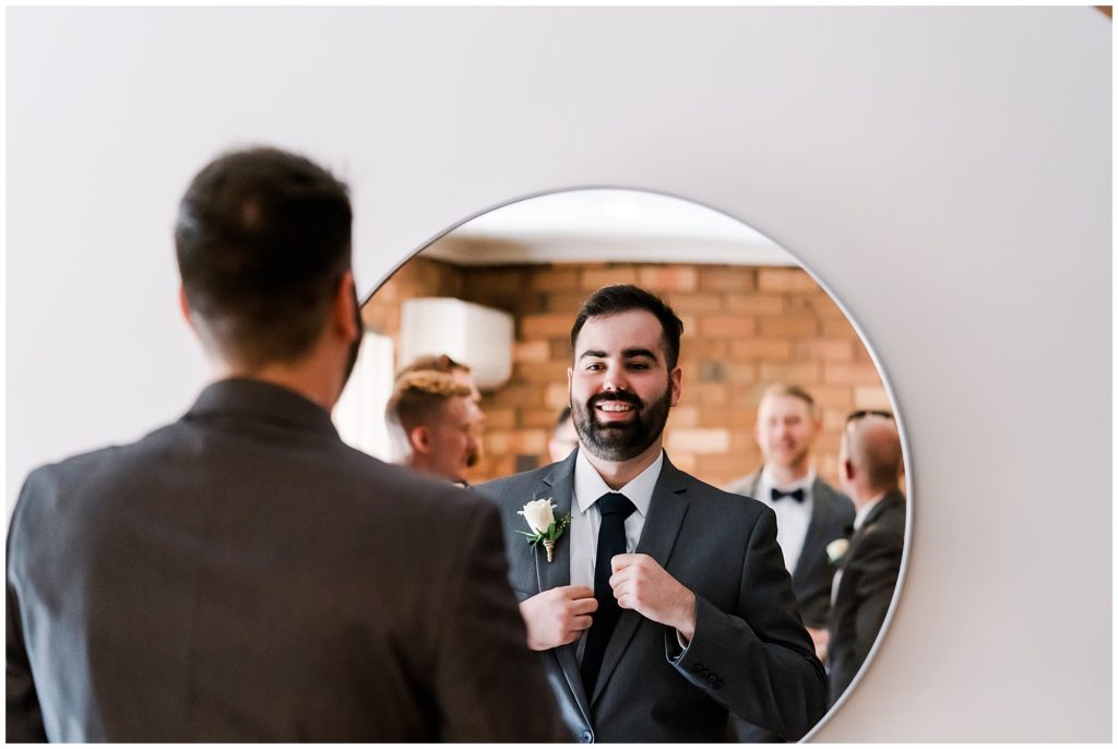 Groom tying his tie while looking in the mirror