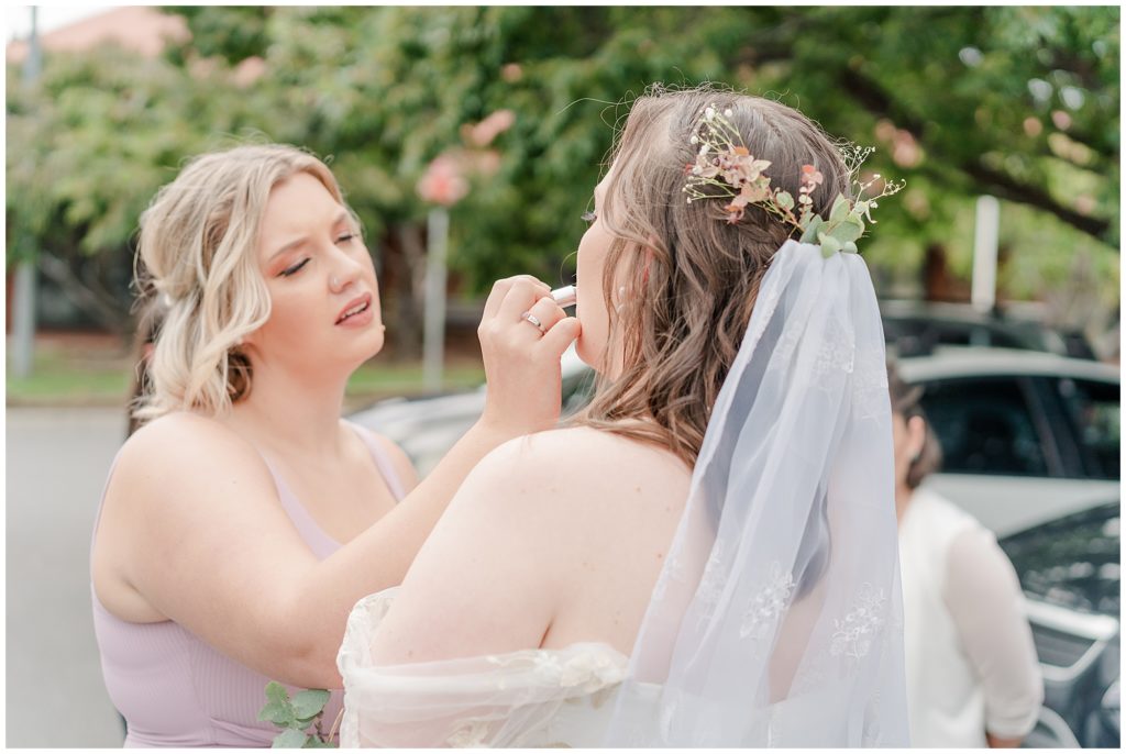 Bride getting her makeup touched- up by her lovely bridesmaid in a pink dress